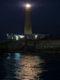 Illuminated built structure by sea against sky at night