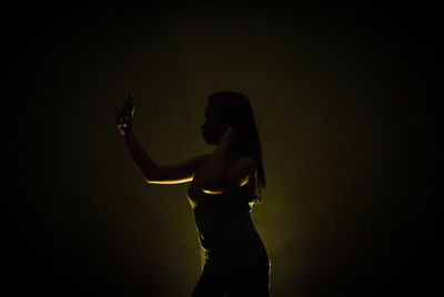 Side view of woman standing against black background