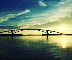 Silhouette bridge over river during sunset