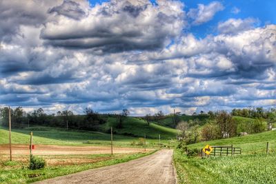 Road by agricultural field against sky