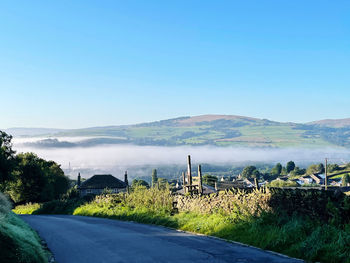 Road amidst field against clear blue sky