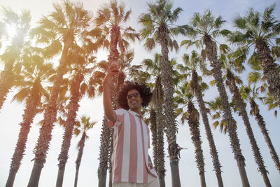 Low angle view of young man standing against palm trees