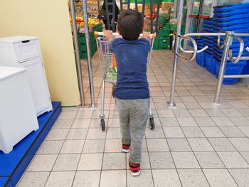 Rear view of boy pushing shopping cart in supermarket