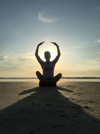 Silhouette person sitting on beach against sky during sunset