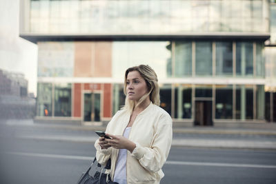 Young woman with mobile phone walking in city