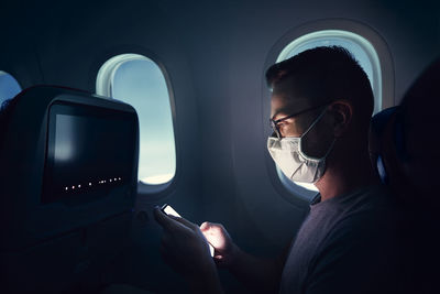 Man with face mask traveling by airplane. passenger using phone during flight.