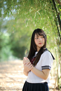 Young woman looking away while standing against plants