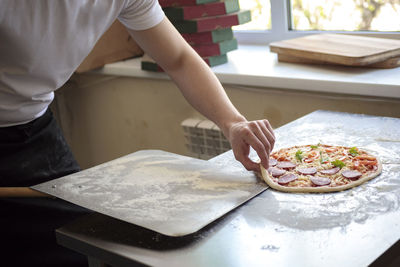 Food cooking, culinary and people concept - cook or baker hand with pizza on peel at pizzeria