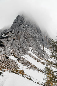 Tiny human walking on snow covered path under magnificent misty mountain