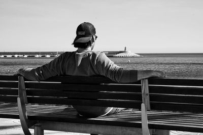 Man sitting on bench looking at sea against sky