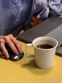 Midsection of man holding coffee cup on table