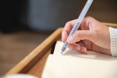 Close-up of female hands writing with gel black pen in leather notepad on wooden table at home
