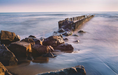 Rocks in sea against sky during sunset