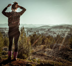 Full length rear view of woman standing on field by city against clear sky