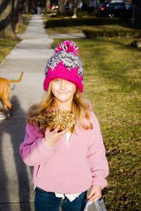 Portrait of smiling girl holding flowers while standing on footpath