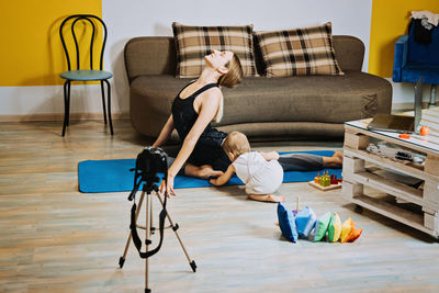 Mother fitness instructor personal trainer record video near camera at home with baby daughter
