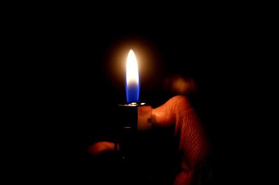 Close-up of hand holding lit candle in darkroom