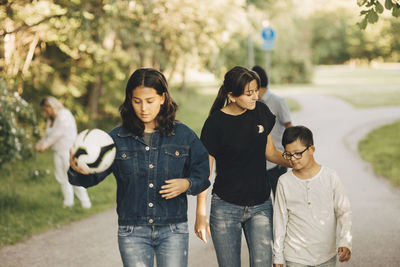 Siblings walking on pathway with parents in background at park