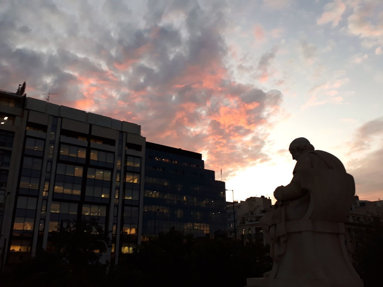 SILHOUETTE STATUE BY BUILDINGS AGAINST SKY AT SUNSET