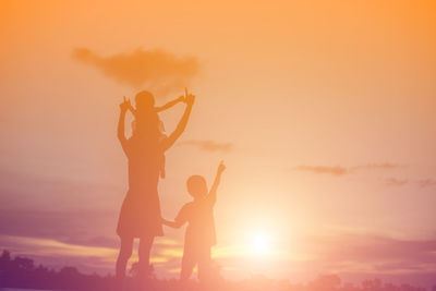 Silhouette friends standing against orange sky