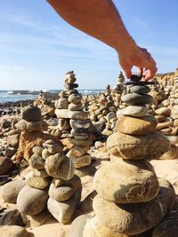 Cropped hand of man stacking pebble at beach against sky