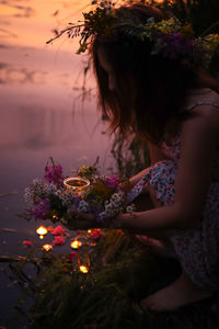 Woman with pink flowers by sea against sky during sunset