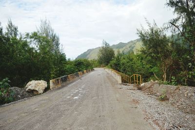 Empty road along trees and plants against sky