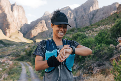 Smiling female hiker checking time on wristwatch in mountain