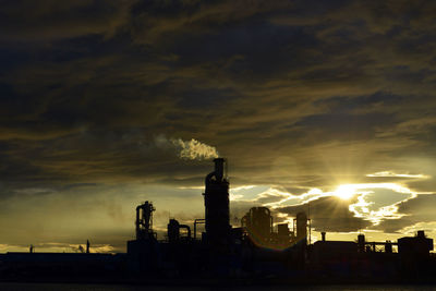 Silhouette factory against sky during sunset