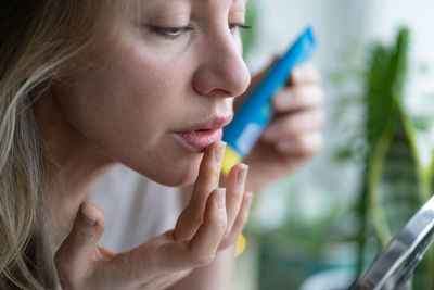 Woman applying lipstick by mirror on table