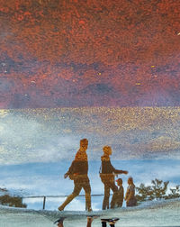 Reflection of people on water against sky