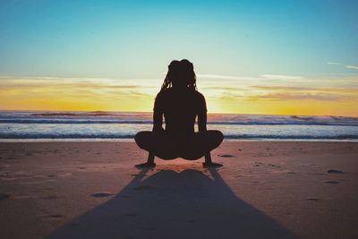 Rear view of woman exercising at beach during sunset