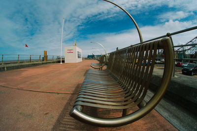 Empty footpath by railing in city against sky