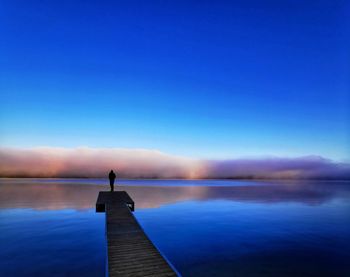 Man standing on pier over lake against blue sky