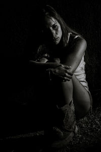 Woman hugging knees while sitting on field at night