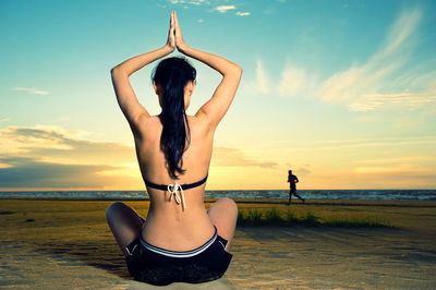 Woman practicing yoga at beach during sunset