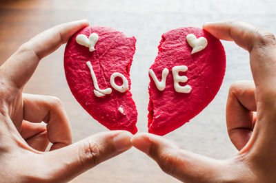 Cropped image of person holding broken heart shape cookie with text