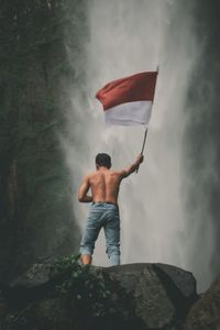 Rear view of man standing on rock with indonesian national flag