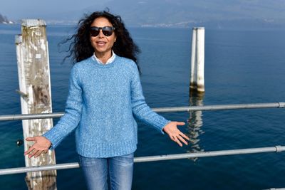 Happy young woman standing by railing against lake