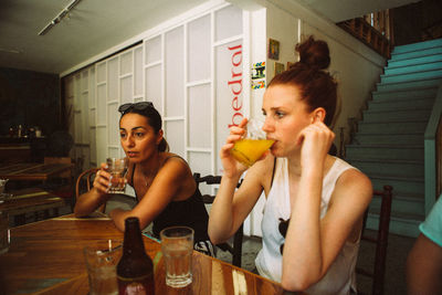Young woman drinking glass while sitting in restaurant