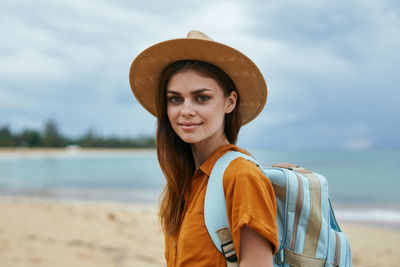 Portrait of smiling young woman standing at beach against sky