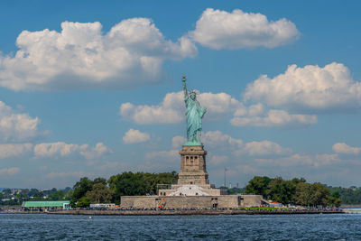 Statue of liberty and liberty island full of tourists on a sunny day with white clouds and blue sky