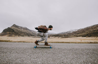 Side view of man skateboarding on road against sky