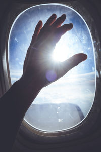 Close-up of hand against sky seen through window