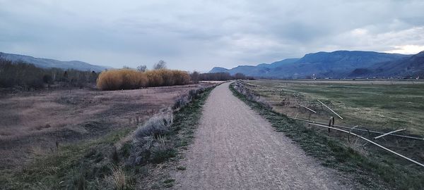 Empty road amidst field against sky