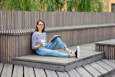 A female blogger in a public place reads a book and rests, drinks coffee and smiles