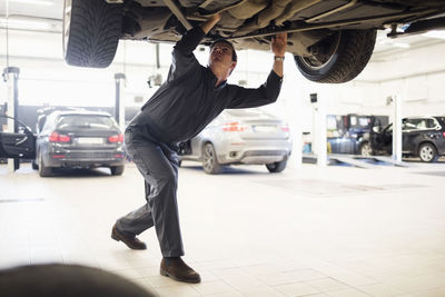 Young mechanic working under car in repair shop