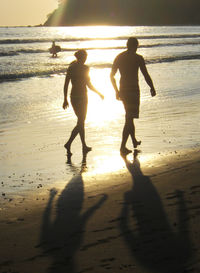 Silhouette people on beach against sky during sunset