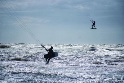 Men surfing in sea against sky