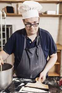 Portrait of young man making dough in commercial kitchen